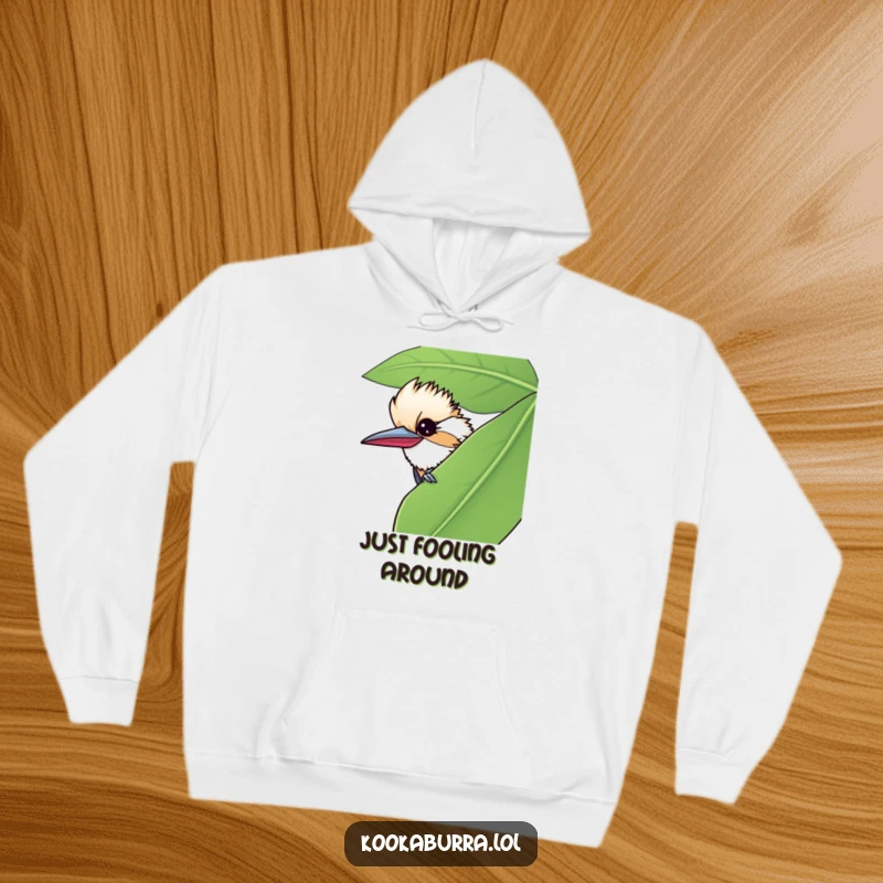 Funny hoodie featuring a kookaburra peeking from behind a large leaf, sharing a mischievous wink for cozy fun.