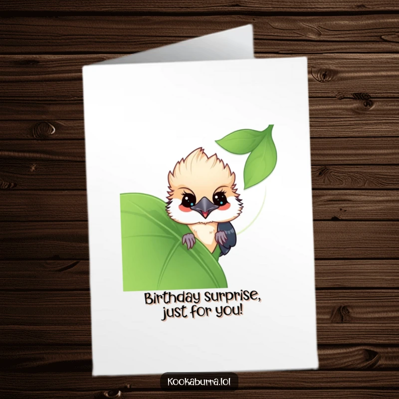 Funny Free Printable Birthday Card showing a kawaii kookaburra playfully peeking from behind a large leaf, ready to share a birthday surprise.
