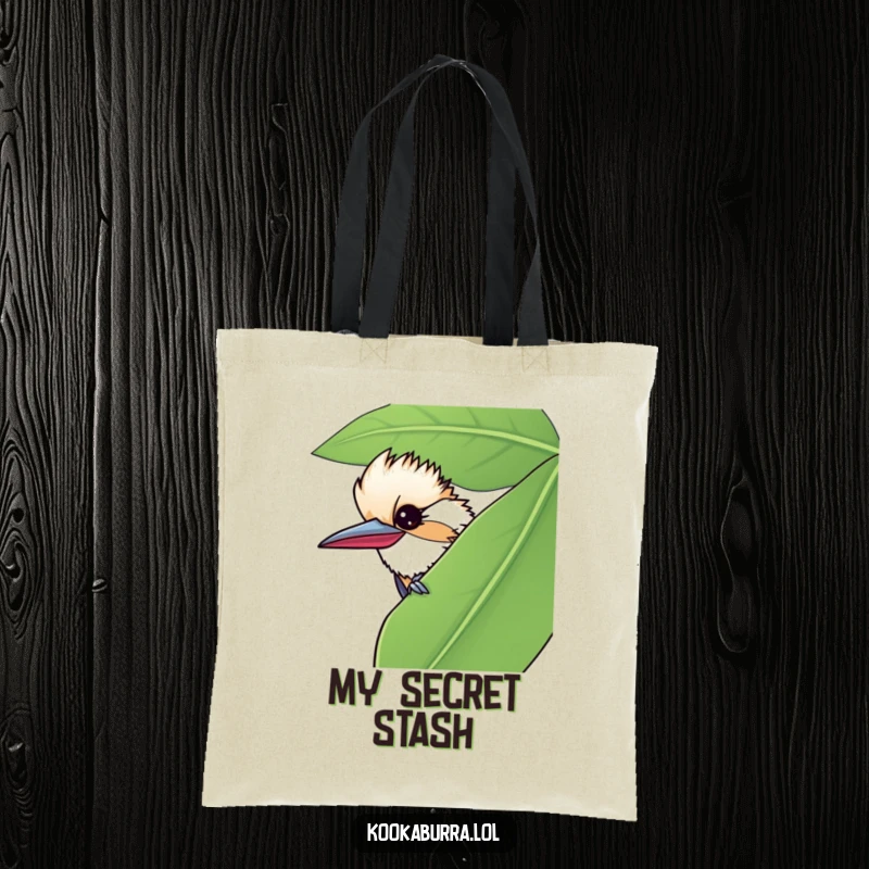 Funny tote bag with a kookaburra peeking from behind a large leaf, giving a mischievous wink, perfect for carry-alls.
